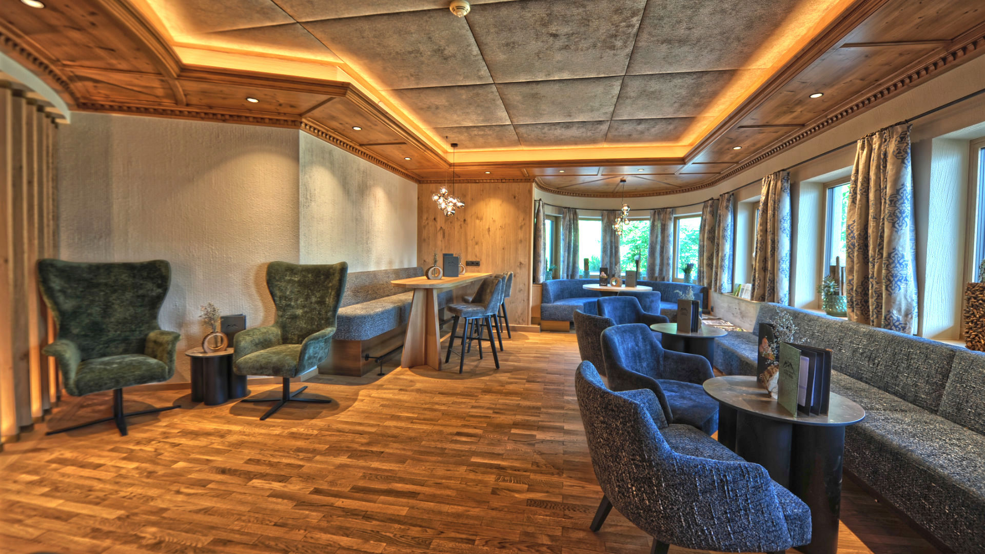 Hotellounge mit Holzboden und Holzdecke, Panoramafenstern, blauen Sesseln, kleinen Tischen und Menükarten