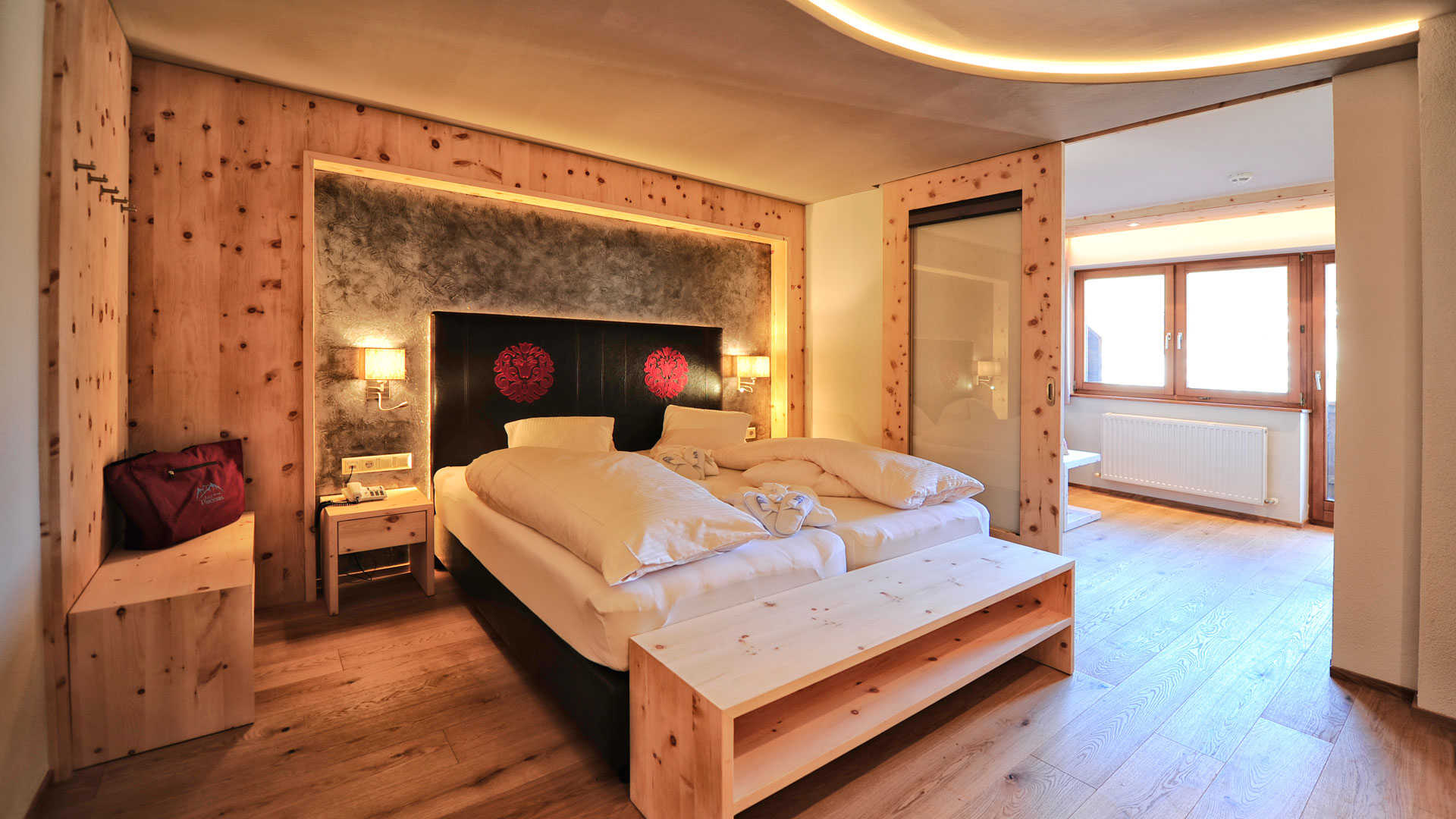 Modernes Hotelzimmer mit Doppelbett, Holzmöbeln und Sitzbereich, gemütlich beleuchtet und mit großen Fenstern im Hintergrund.